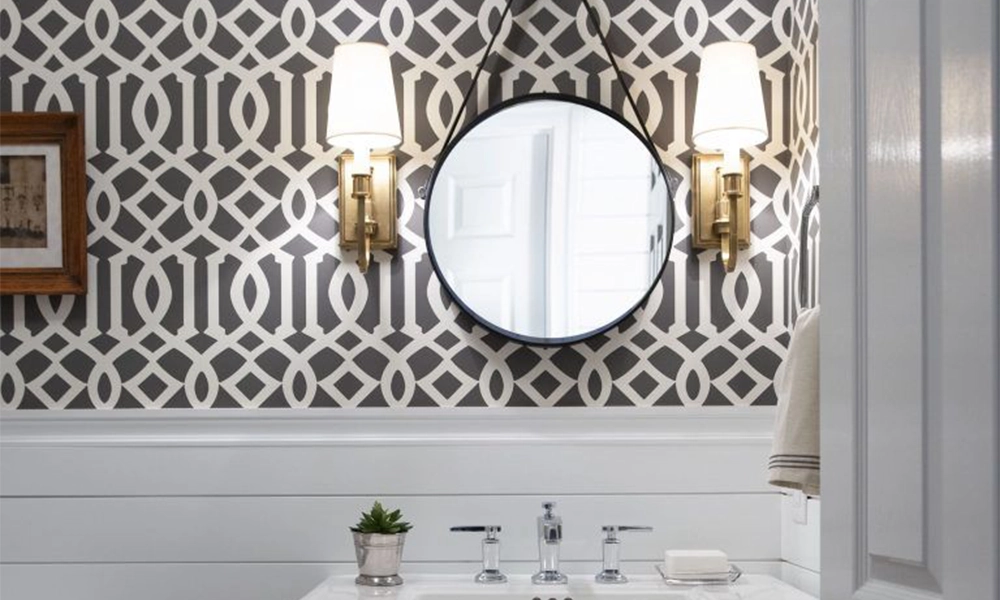 Bathroom with geometric pattern tiles on the wall, a round mirror, wall-mounted lighting, and a modern sink with silver faucets. The combination of bold patterns and minimalistic design creates a stylish, contemporary look