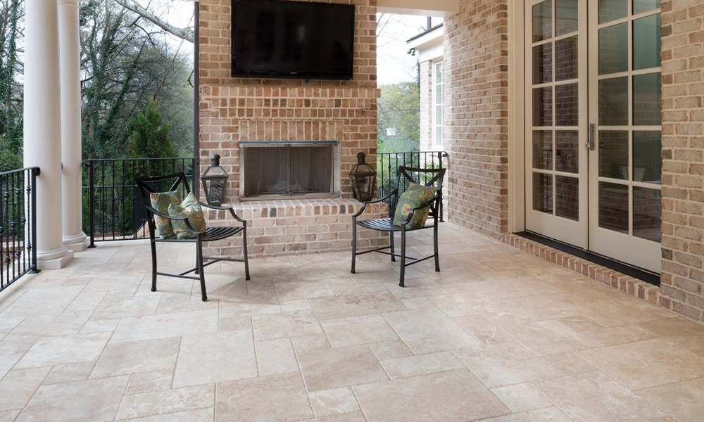 Outdoor patio with beige travertine pavers and brick fireplace, elegant natural stone flooring design.
