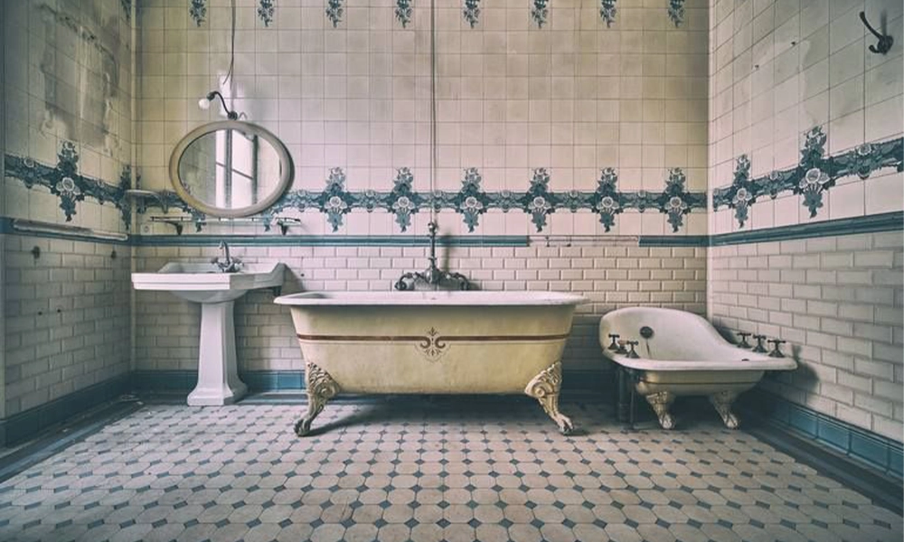 "Vintage bathroom with classic white tiles and floral blue accents, featuring an old-fashioned clawfoot bathtub and a pedestal sink. The hexagonal tile floor and vintage mirror add to the nostalgic charm of the space."