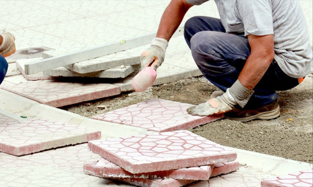 A worker is placing the last pavers in a row, using a mallet to tap them into position, making sure the edges are properly aligned for a smooth and stable finish.