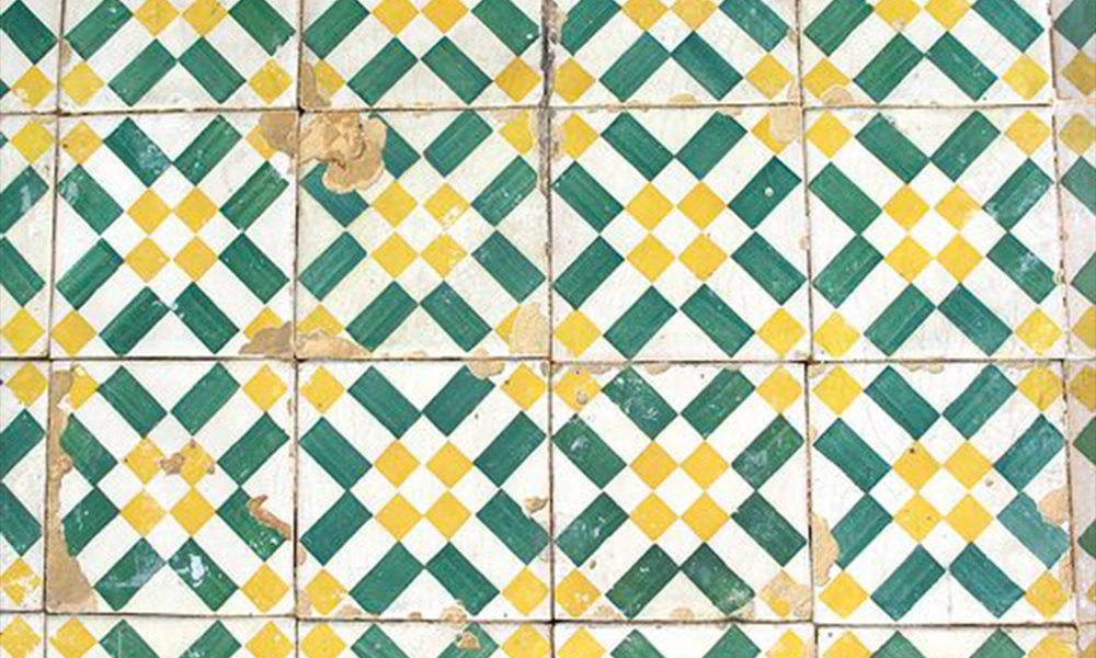 A vintage tile pattern with green and yellow diamond shapes on a white background, showing some wear and tear.