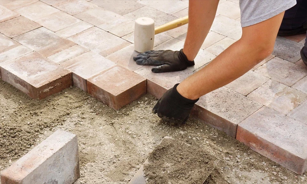 A worker carefully places pavers in a pattern, using a rubber mallet to ensure they are securely set into place, creating a strong and even surface.
